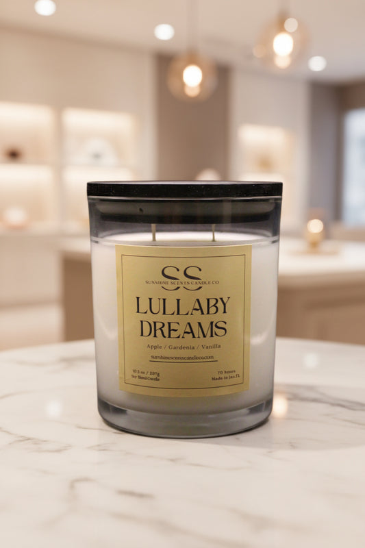 A double-wick jar candle labeled 'Lullaby Dreams' by Sunshine Candle Co sits on a light marble countertop with a softly blurred boutique interior in the background.