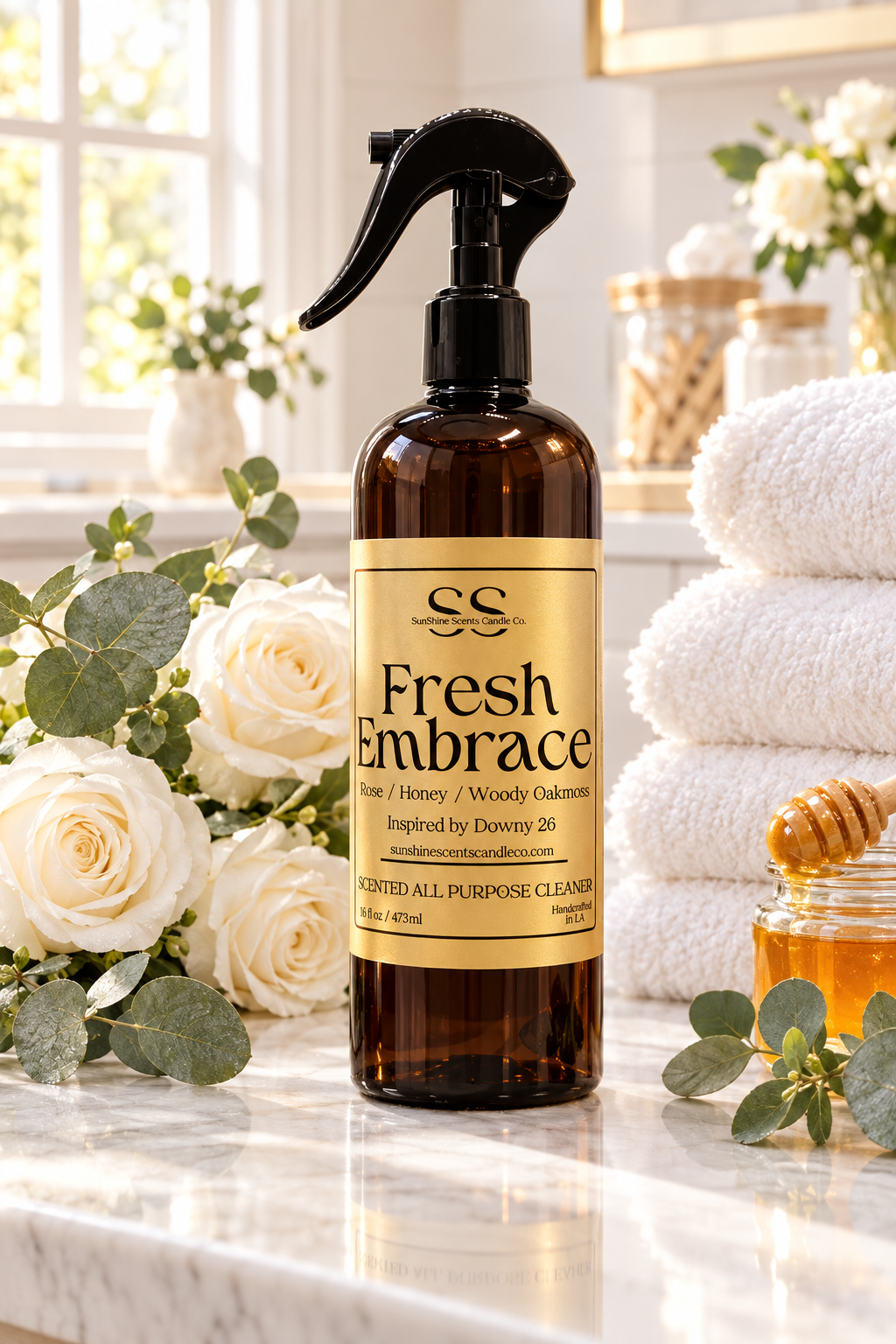 “SunShine Scents Candle Co. Fresh Embrace All Purpose Cleaner 16oz spray bottle on a marble counter beside white roses, towels and honey.”