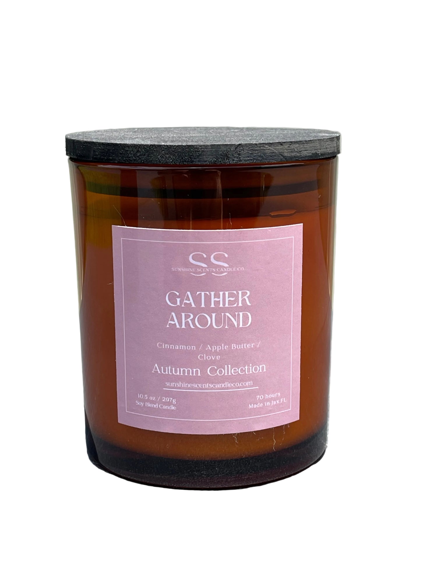 An amber glass jar candle with a dusty pink label reading 'GATHER AROUND' and 'Autumn Collection' by SS Candle Co, resting on a gray textured surface.
