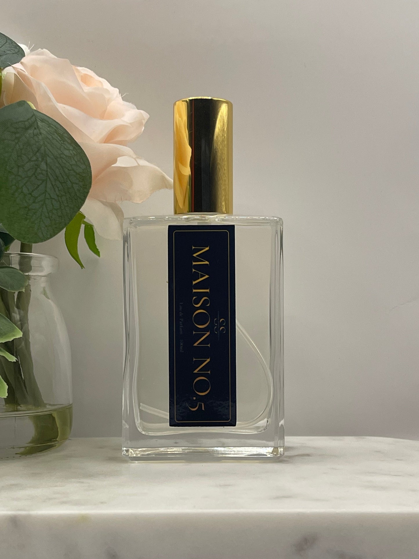 A clear rectangular perfume bottle with a black label reading 'MAISON NO.5' in gold lettering, topped with a shiny gold cap.