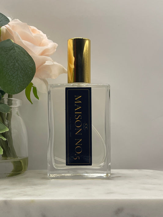 A clear rectangular perfume bottle with a black label reading 'MAISON NO.5' in gold lettering, topped with a shiny gold cap.