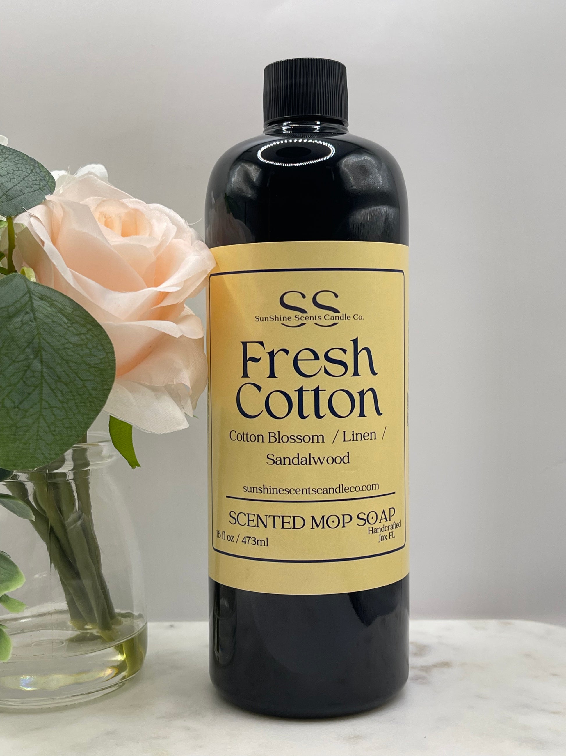 “SunShine Scents Candle Co. Fresh Cotton Mop Soap 16oz bottle with a yellow label beside a pale rose in a glass vase.”